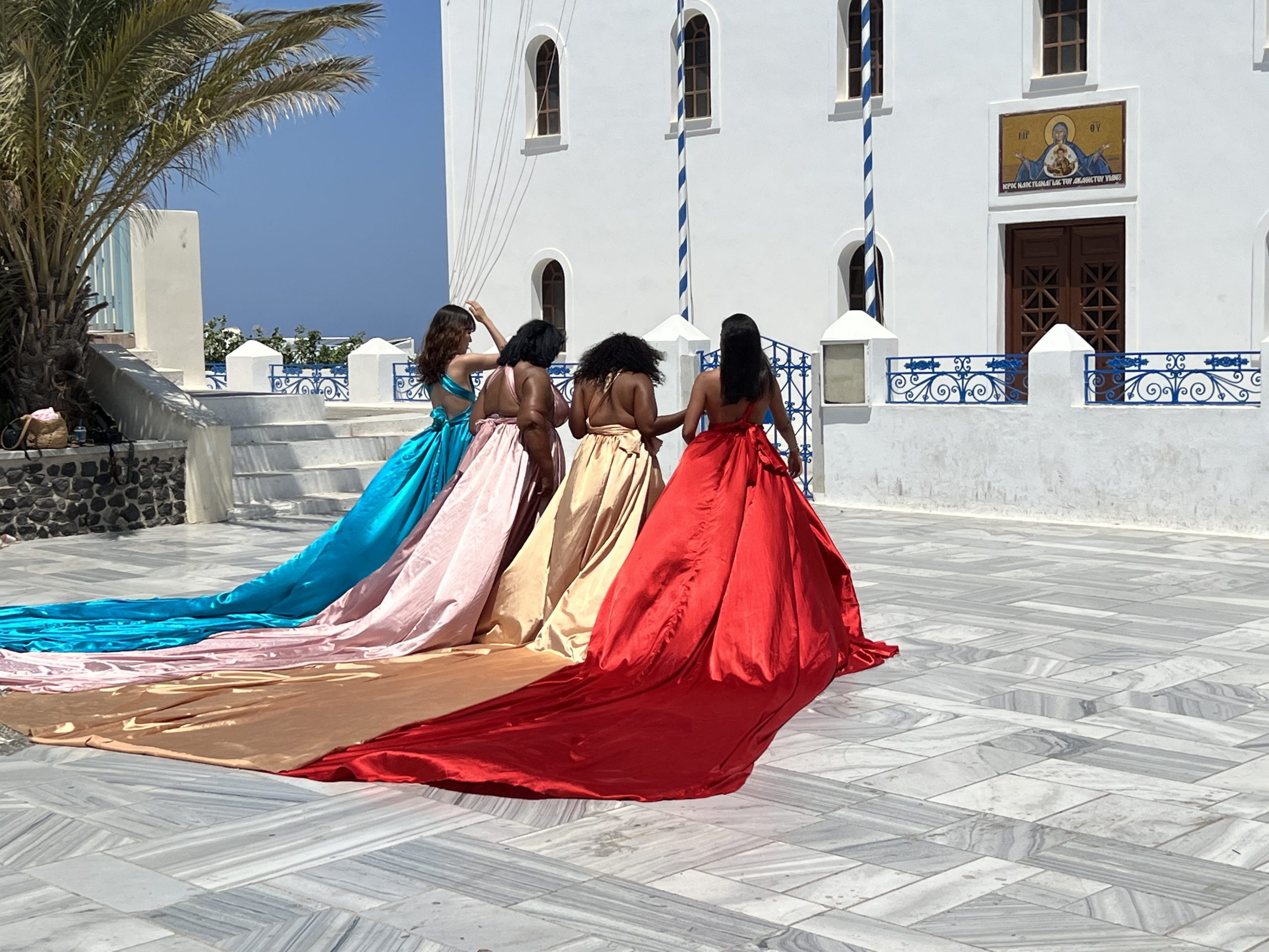 Four women in long dresses sitting on a stone floor.