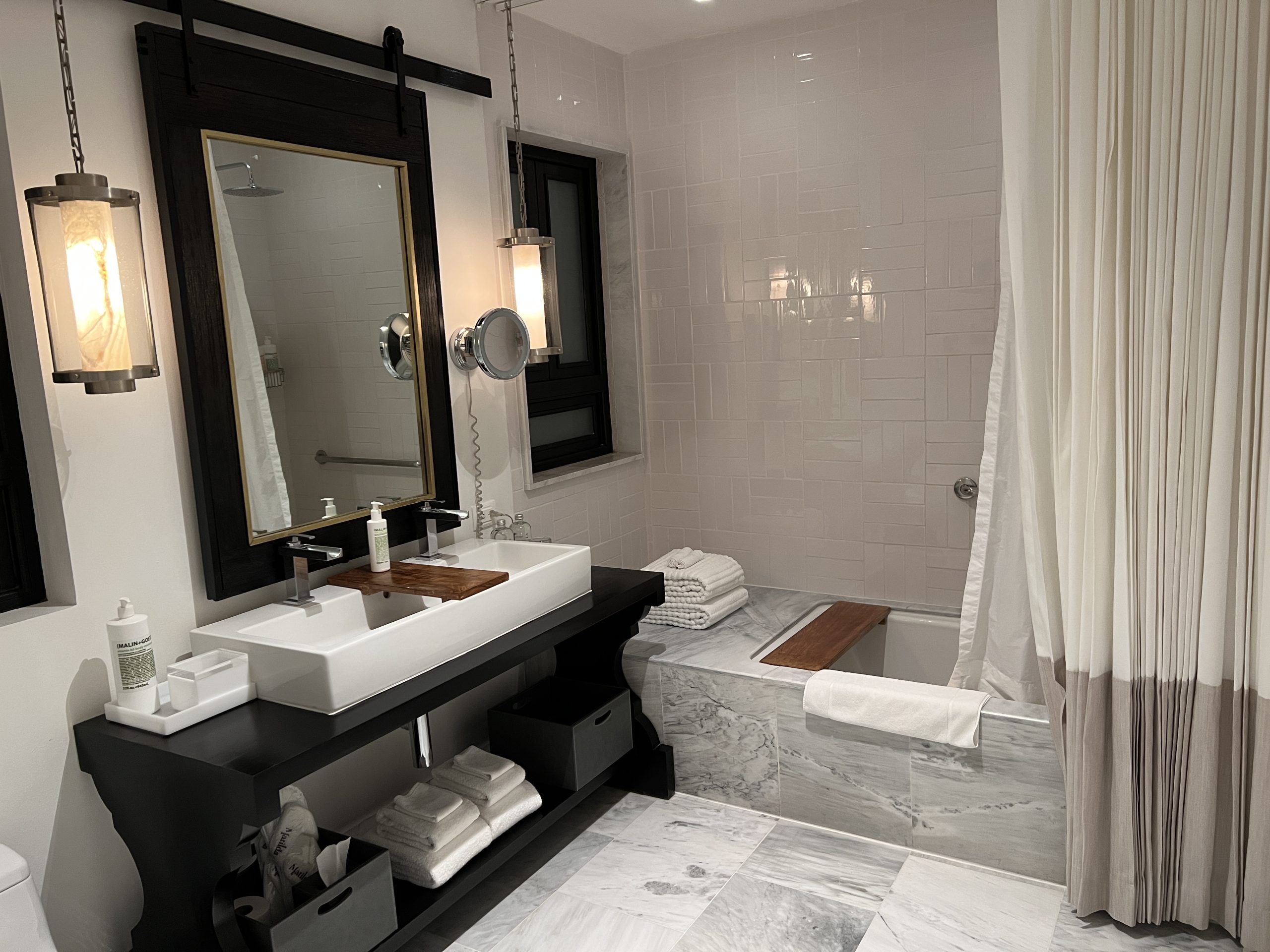 A bathroom with marble floors and walls, a sink, mirror and bathtub.