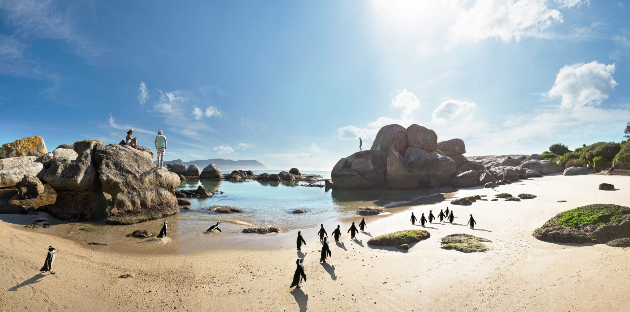 A group of people walking on the beach near some rocks