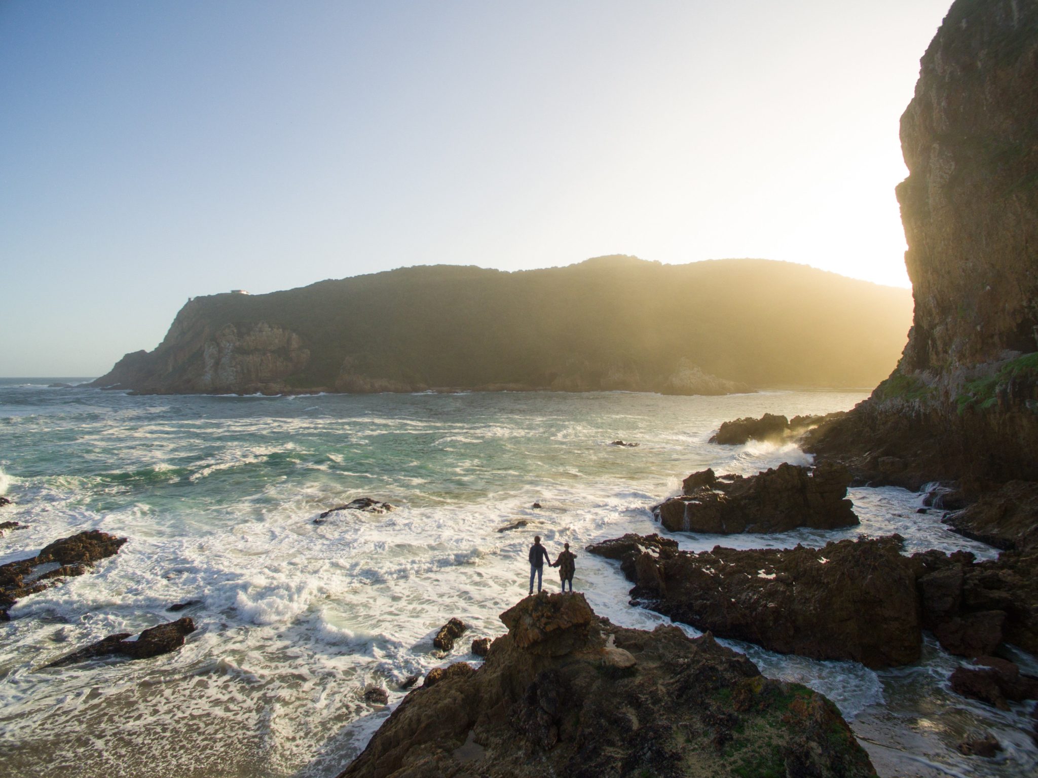 Two people standing on a rock near the ocean.