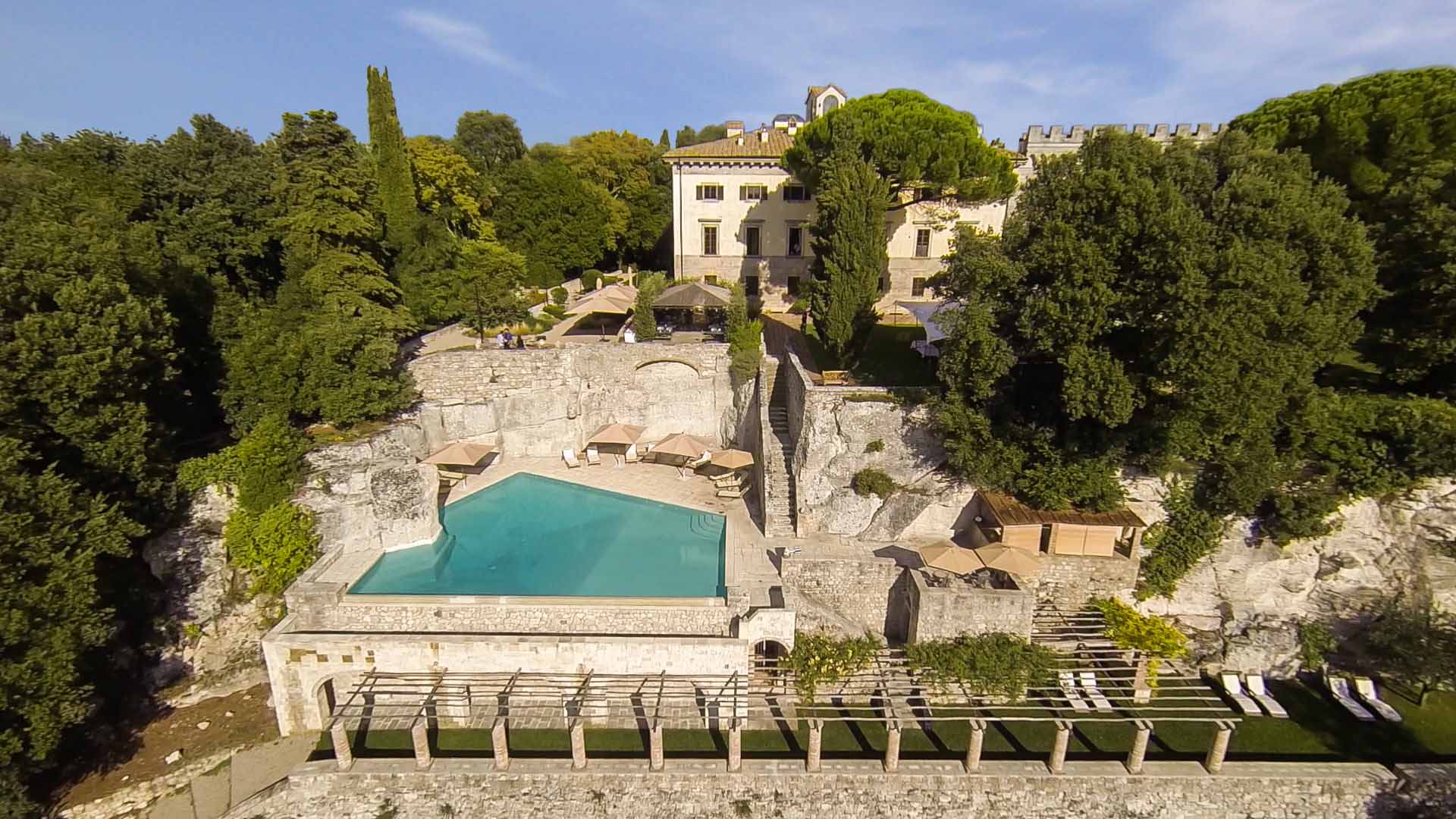 A pool with a stone wall and trees in the background.