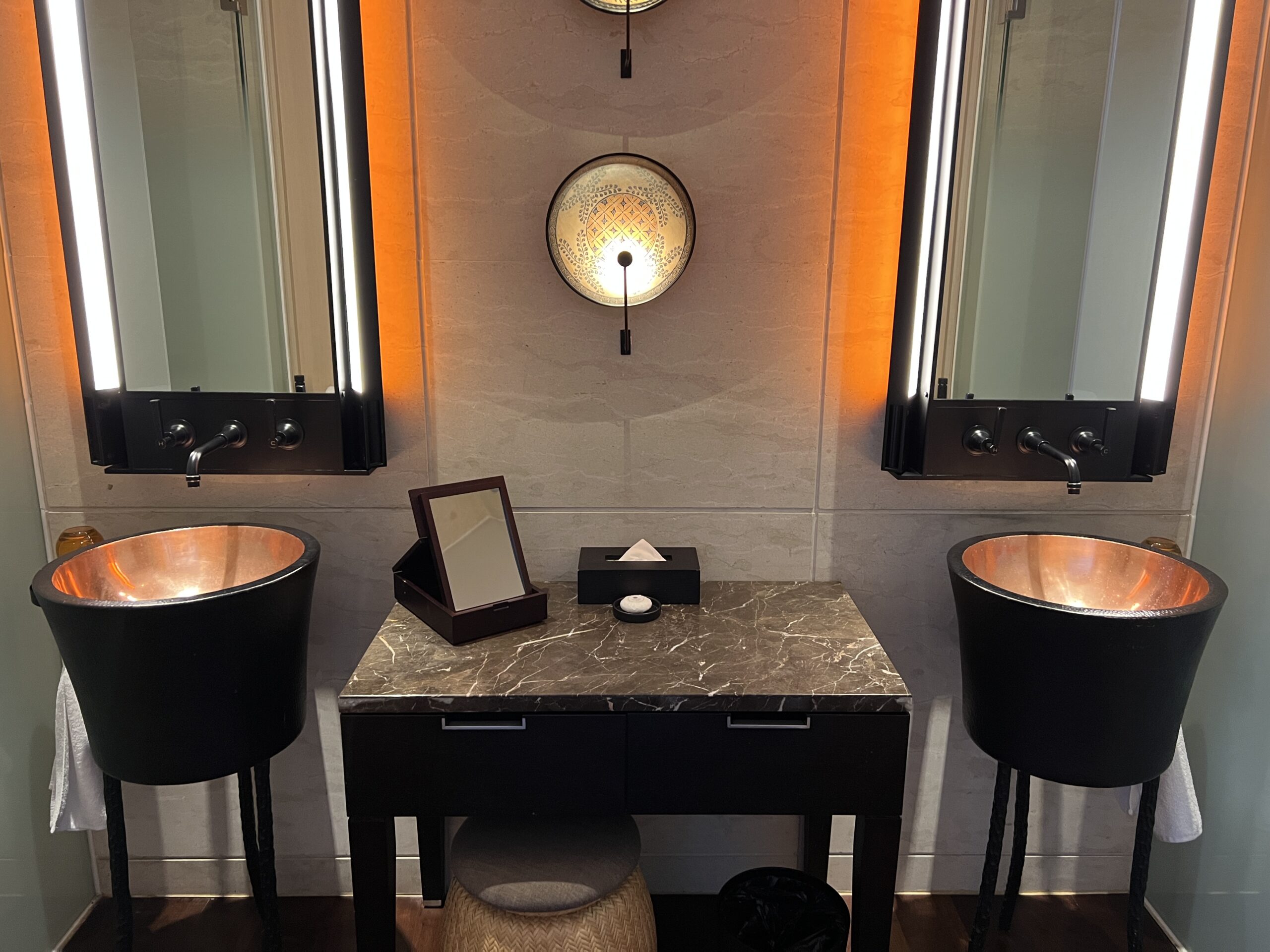 A bathroom with two sinks and mirrors, one of which has lights on.