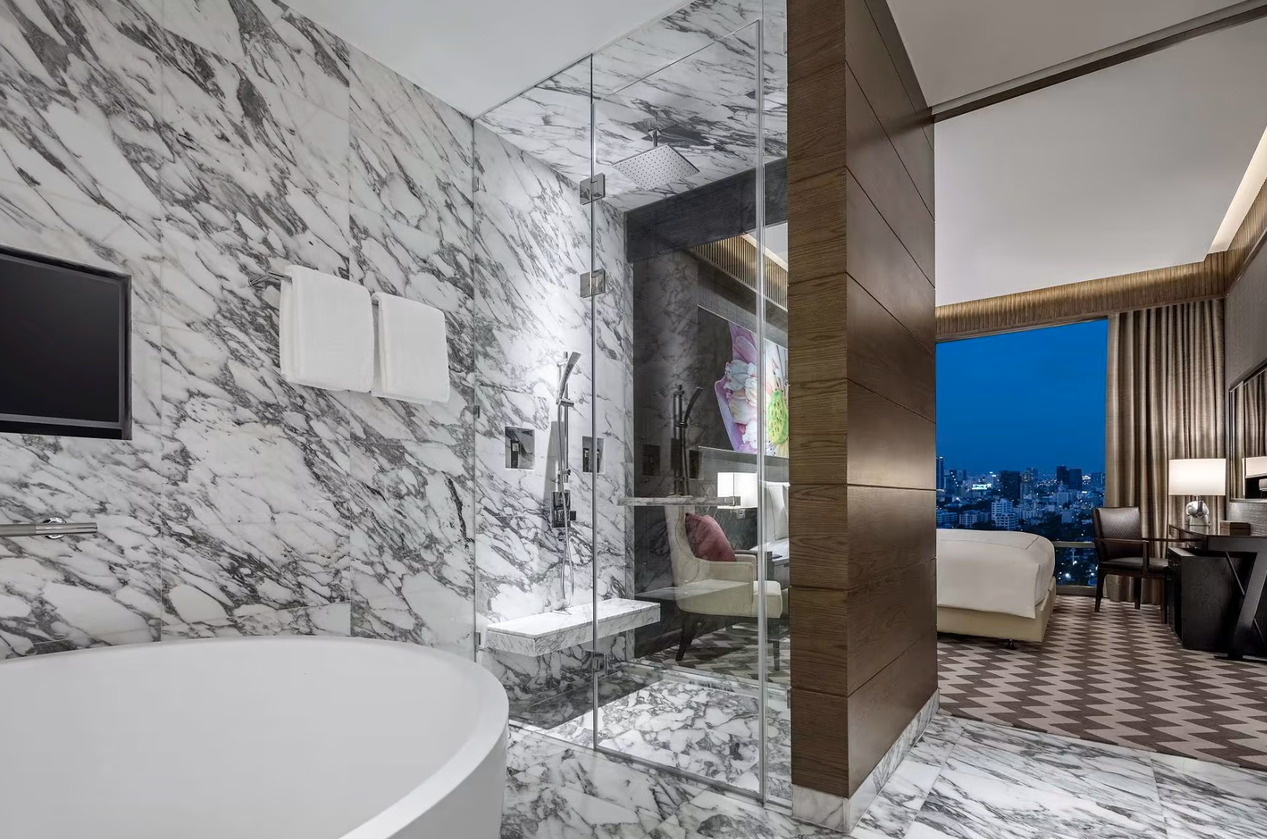 A bathroom with marble walls and floors, and a large glass shower.