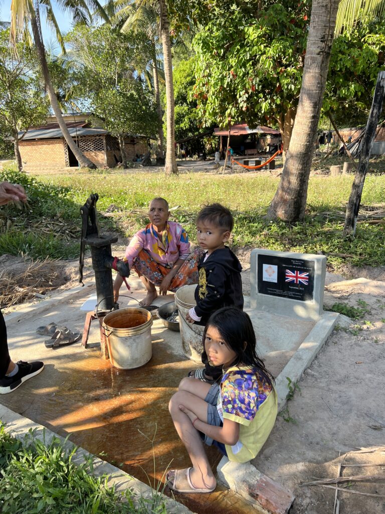 Three children sitting on the ground near a pot.