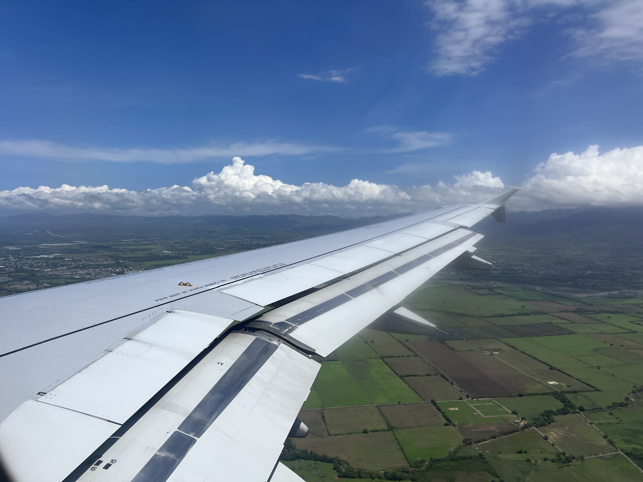 A view of the wing of an airplane flying over a field.