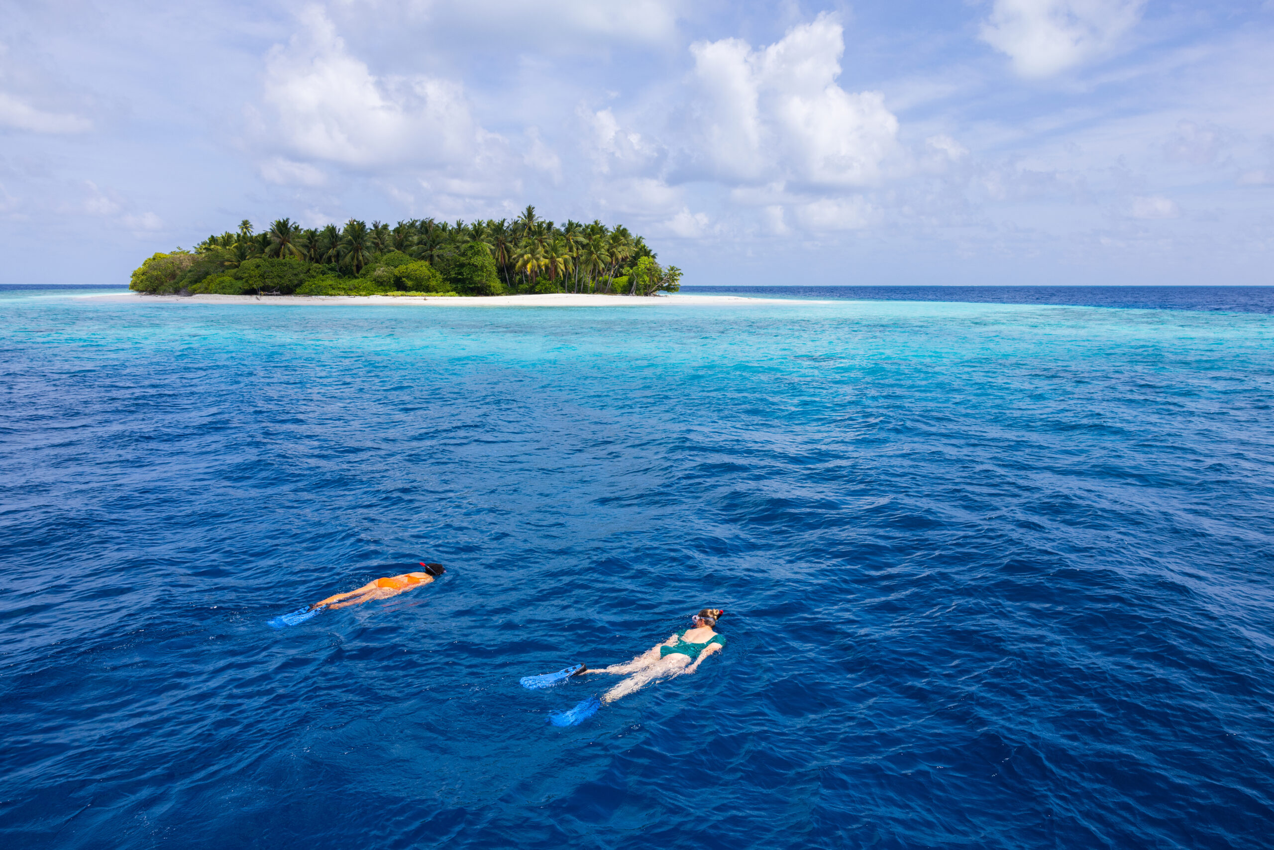 Two people swimming in the ocean with a small island in the background.