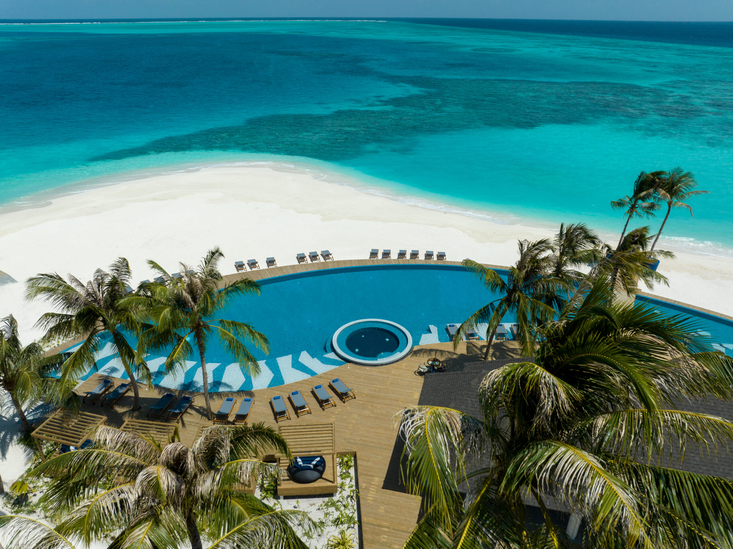 A view of the ocean from above shows an aerial view of a resort pool and beach.