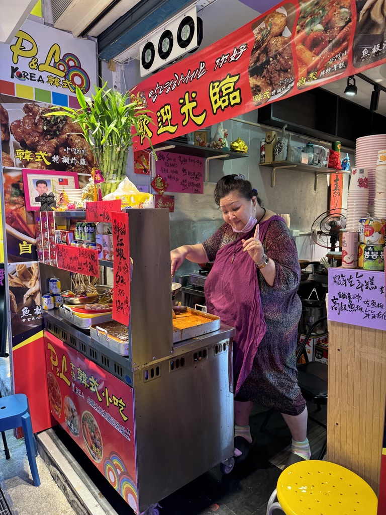 A woman standing in front of an asian food cart.